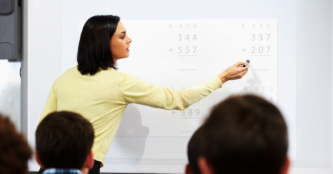 Teacher pointing at mathematics questions on a projector screen in a classroom